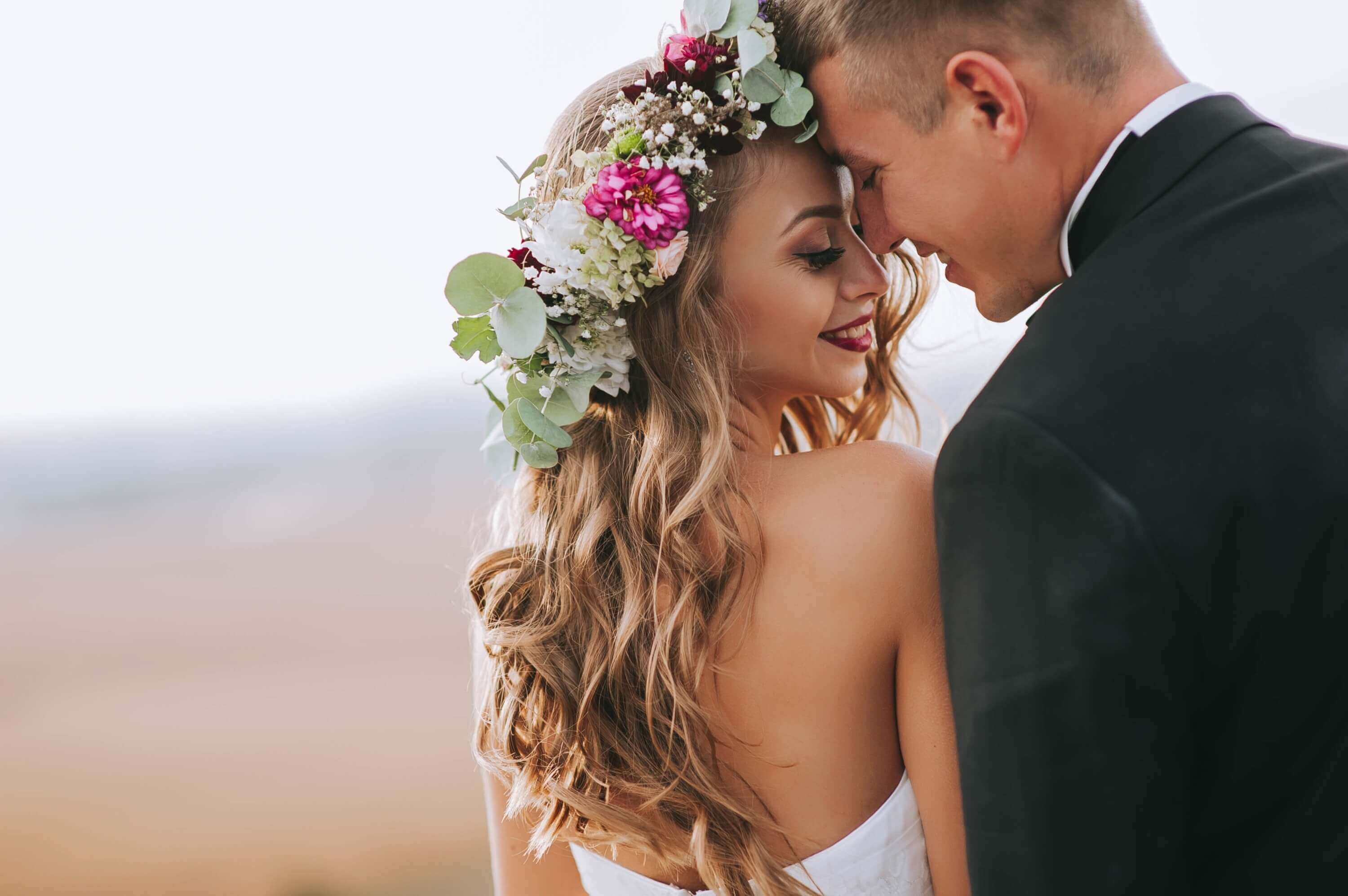 Bride smiling wearing a floral crown cuddling with groom